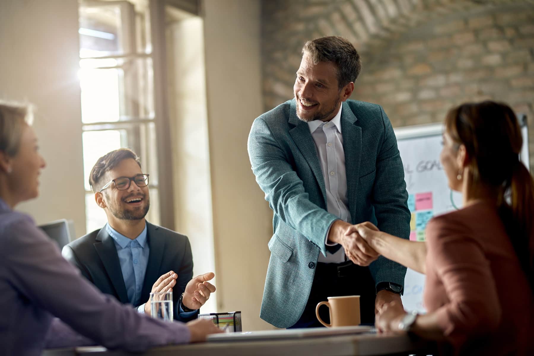 Happy businessmen greeting his colleagues on a meeting and shaking hands with one of them in the office.